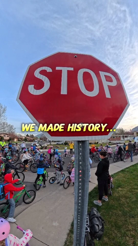A large group of kids and adults with bikes gathered near a stop sign.