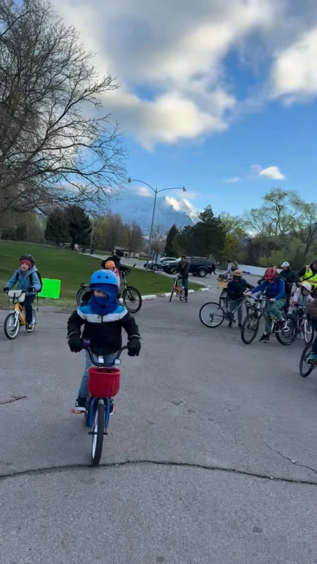 A group of kids and adults gathering with bikes near a park.