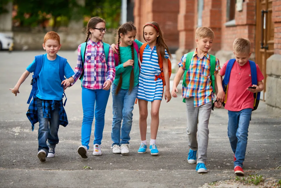 Kids wearing backpacks walking together outside a school.